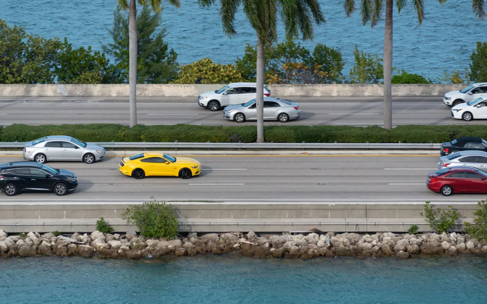 Aerial view of cars driving on a coastal highway lined with palm trees