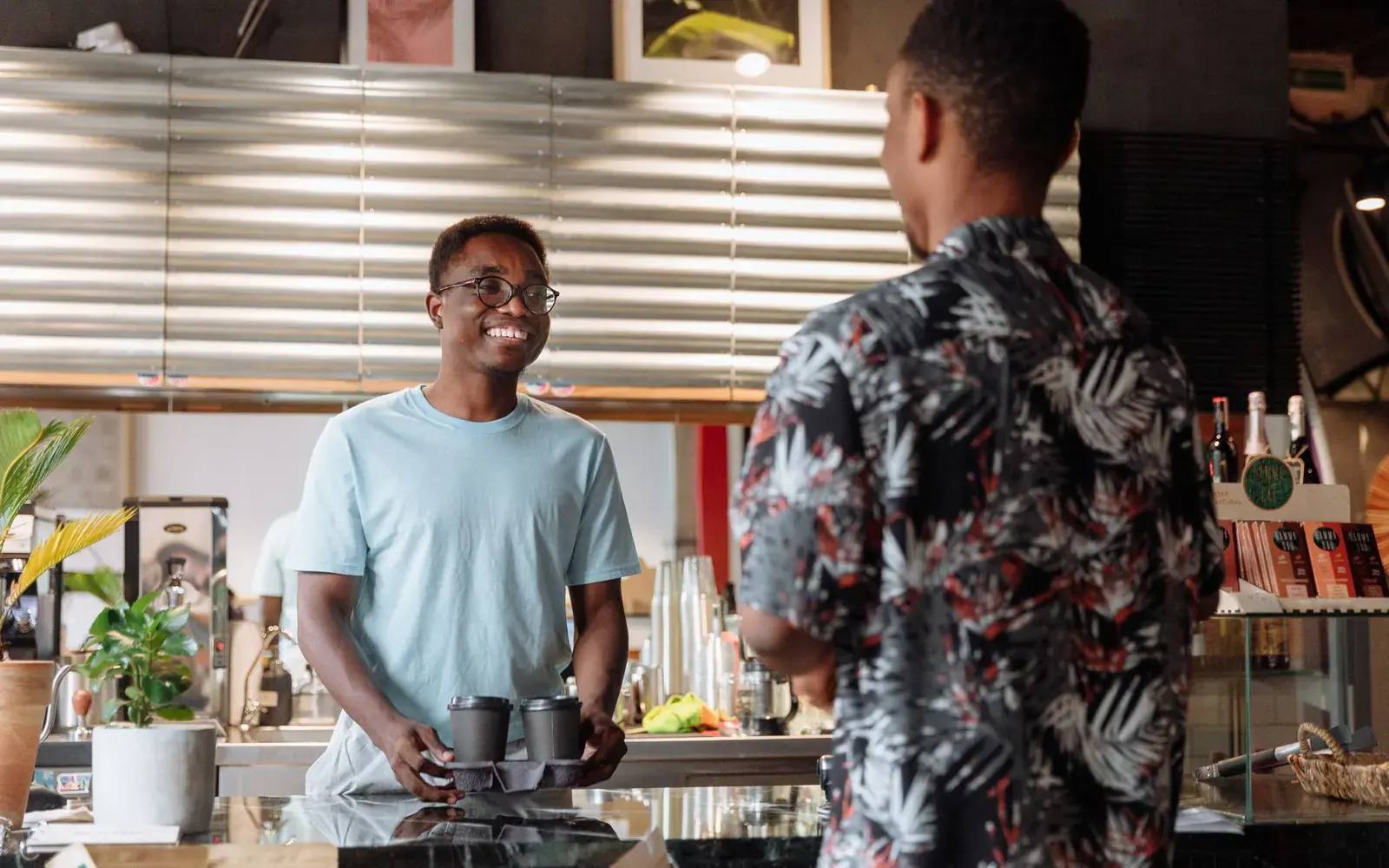 Smiling cafe worker handing coffee to a customer at the counter of a modern small business